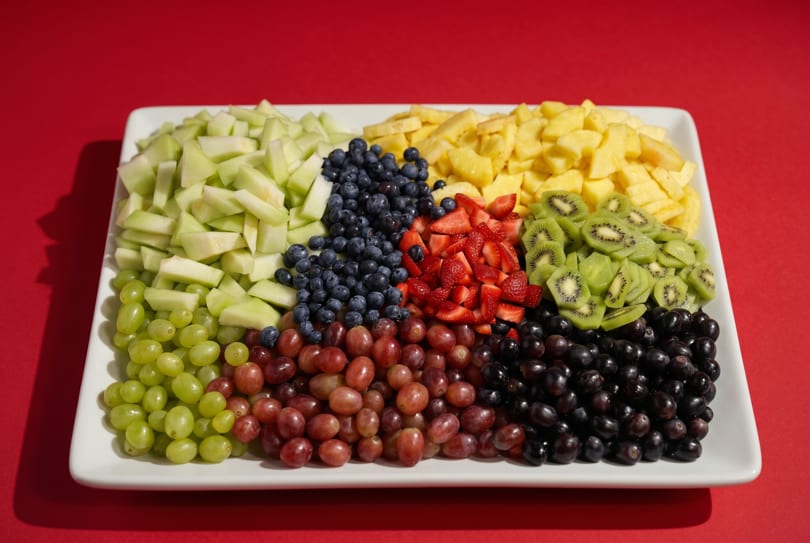 A white platter filled with colorful fresh fruit, including melon, pineapple, blueberries, strawberries, kiwi, and grapes.