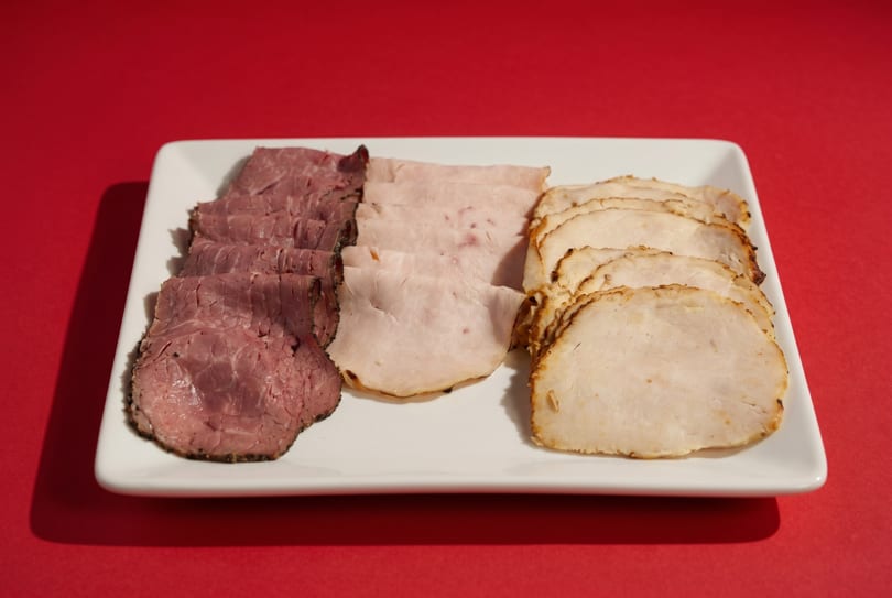 A white rectangular platter holds three rows of sliced deli meats: roast beef, ham, and turkey.