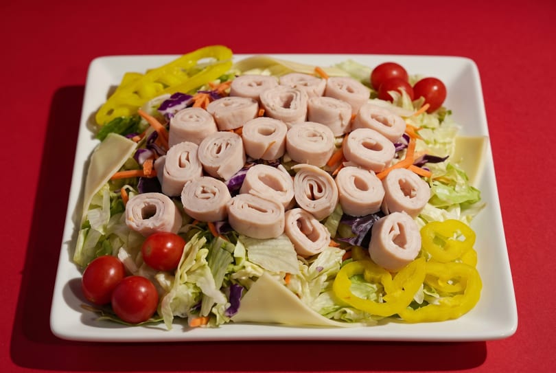 A chef salad with rolled turkey, cherry tomatoes, yellow peppers, and cheese on a white plate.