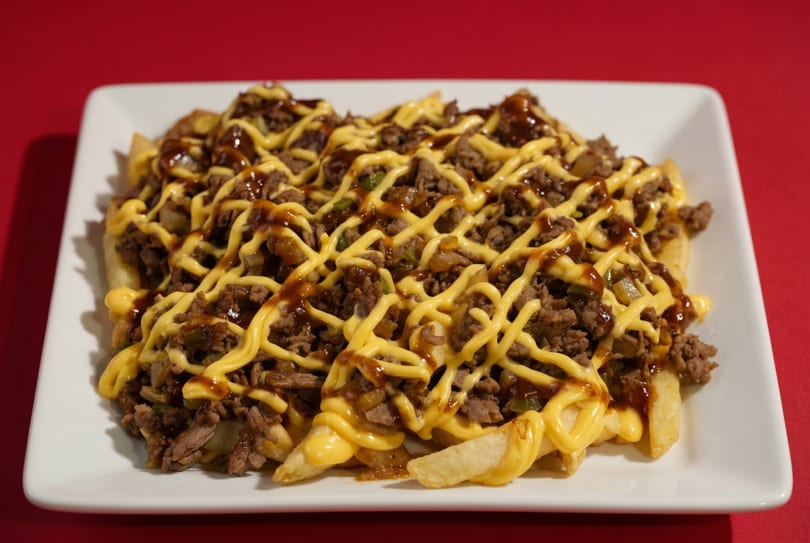 A white rectangular plate filled with golden french fries, topped with ground beef, cheese sauce, and gravy.