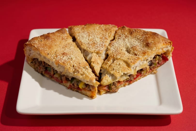 Three slices of a calzone filled with meat and vegetables, topped with parmesan cheese, on a white plate.